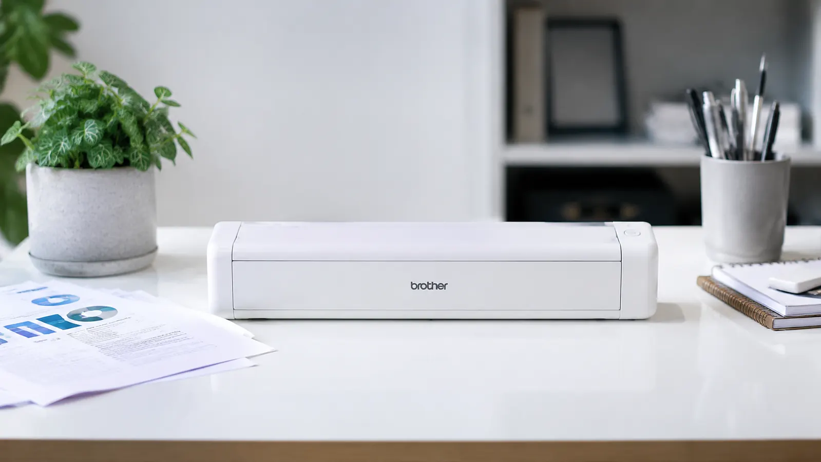 Brother DS-740D portable document scanner on a minimal desk with a scattered stack of business documents ready to feed