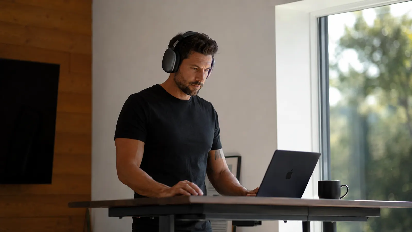 Entrepreneur at a standing desk wearing over-ear headphones, focused on a laptop in a bright modern home office