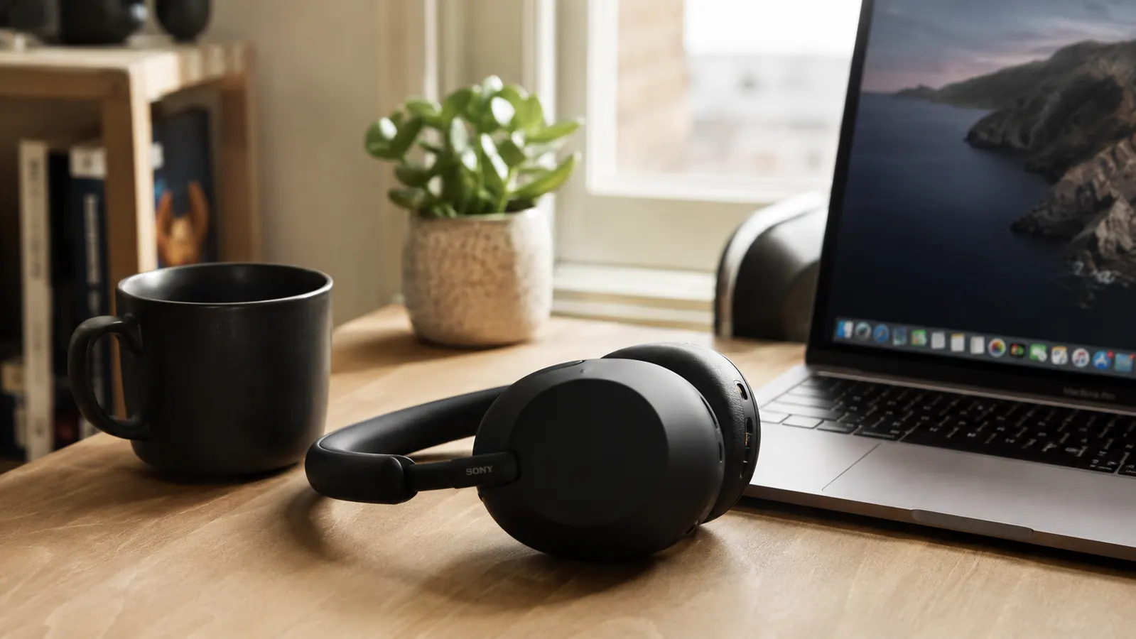 Sony WH-1000XM5 headphones on a clean wooden desk next to a laptop and coffee in a bright home office